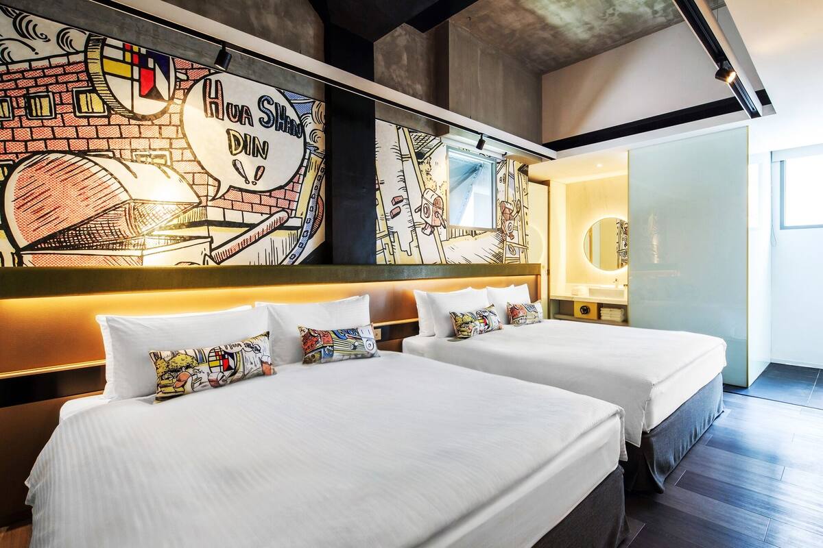 A hotel room with two beds, a mural on the wall, and a modern bathroom.