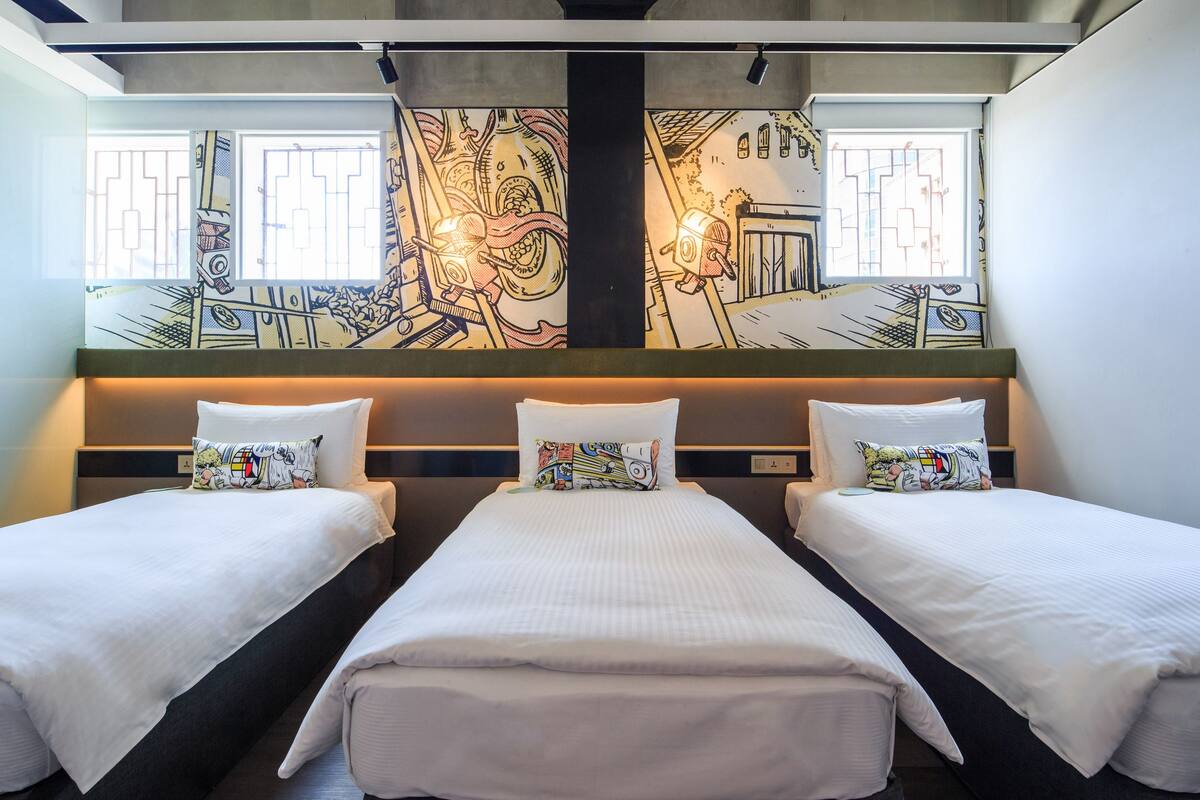 A hotel room with three single beds, a large window with a view, and a mural on the wall.