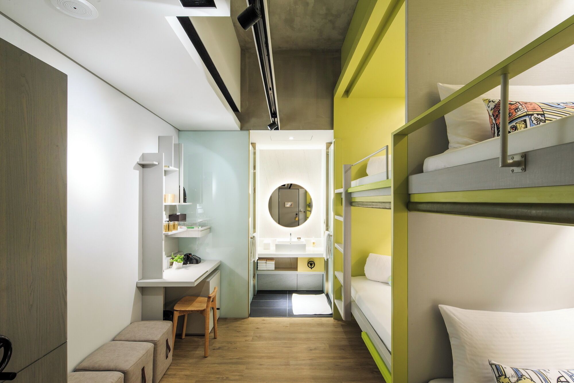 A compact hotel room with bunk beds, a small desk, and a round mirror.