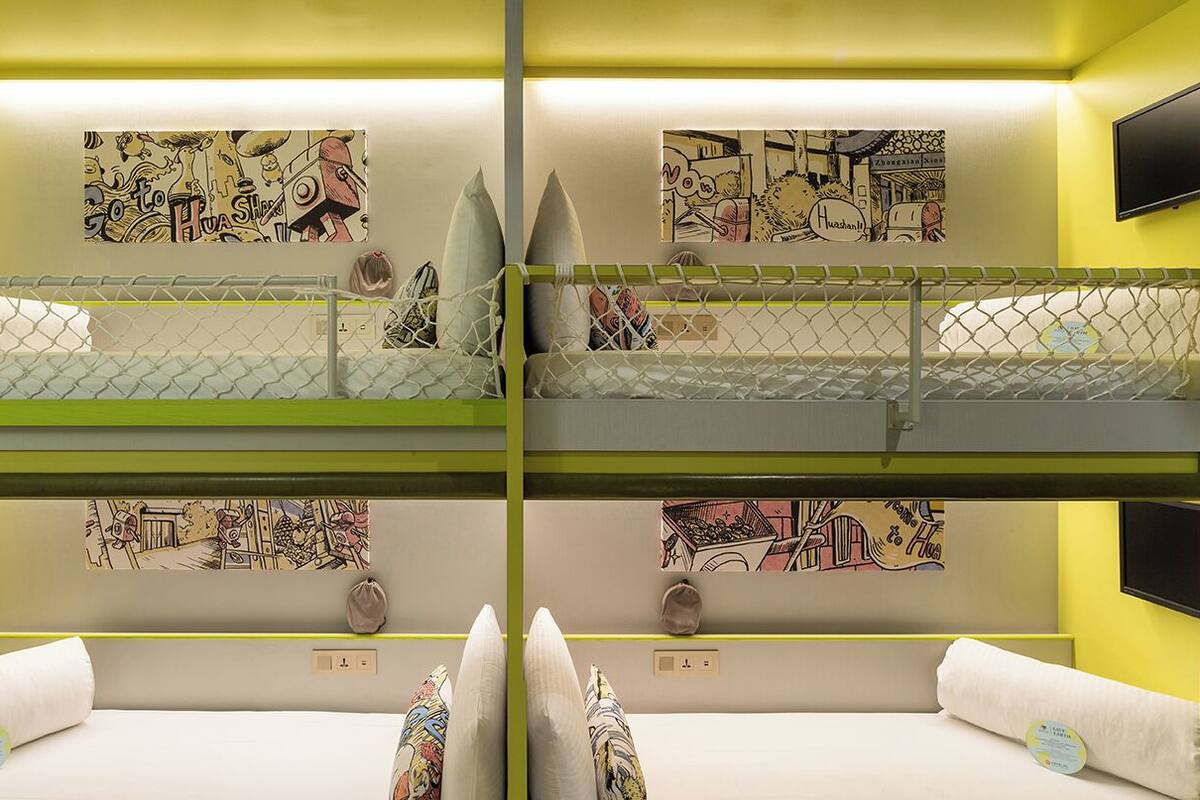 A bunk bed room with two TVs, artwork on the walls, and a bright yellow color scheme.