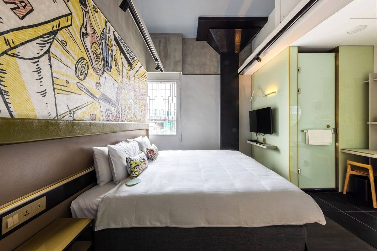A modern hotel room with a large bed, a television, a desk, and a bathroom with a glass shower.
