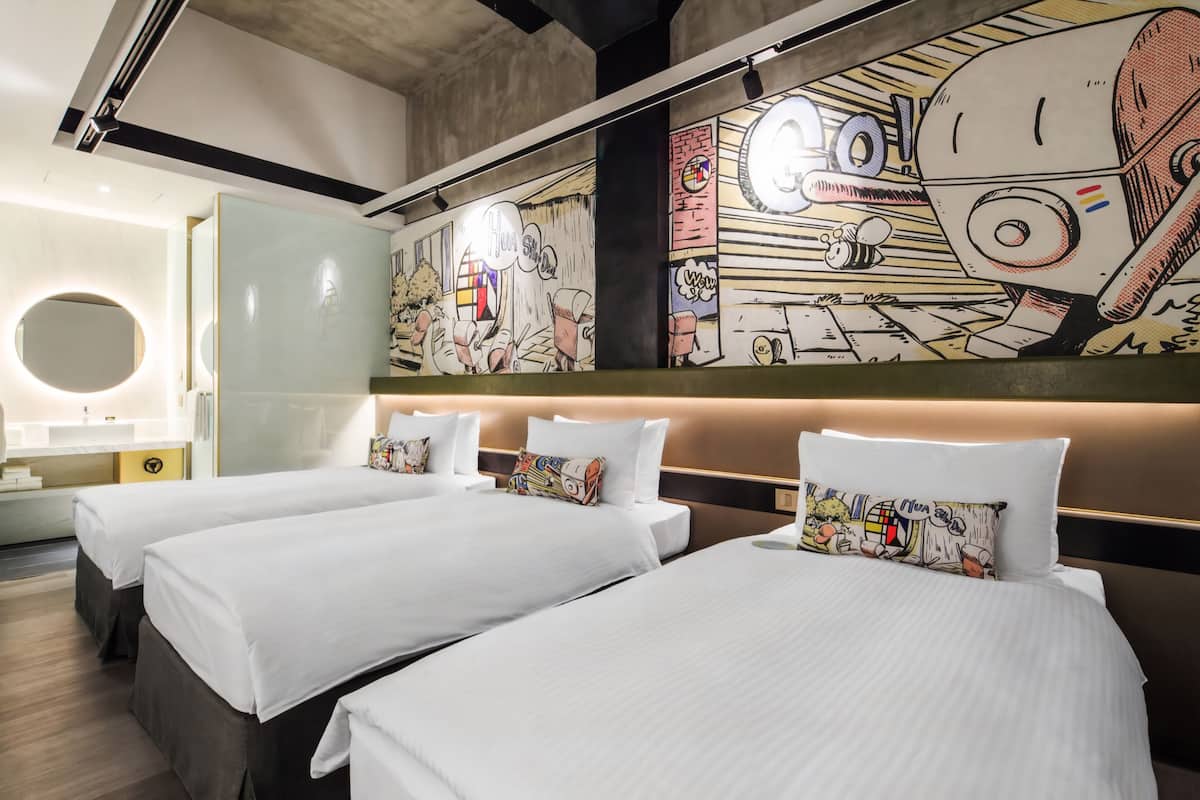 A hotel room with three beds, a large mural on the wall, and a modern bathroom.