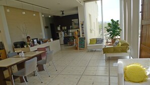 Een ruime woonkamer met een eettafel, stoelen, een bank en een salontafel. Er is een groot raam dat natuurlijk licht en uitzicht op de omgeving biedt.