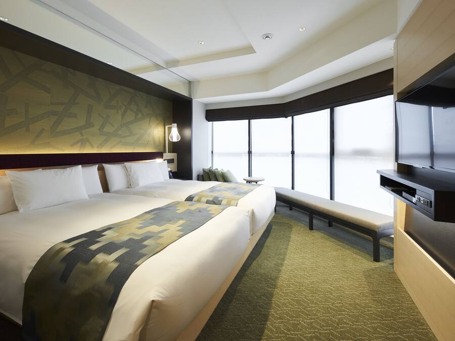 Habitación de hotel con dos camas, un ventanal grande, un televisor de pantalla plana y una banca.