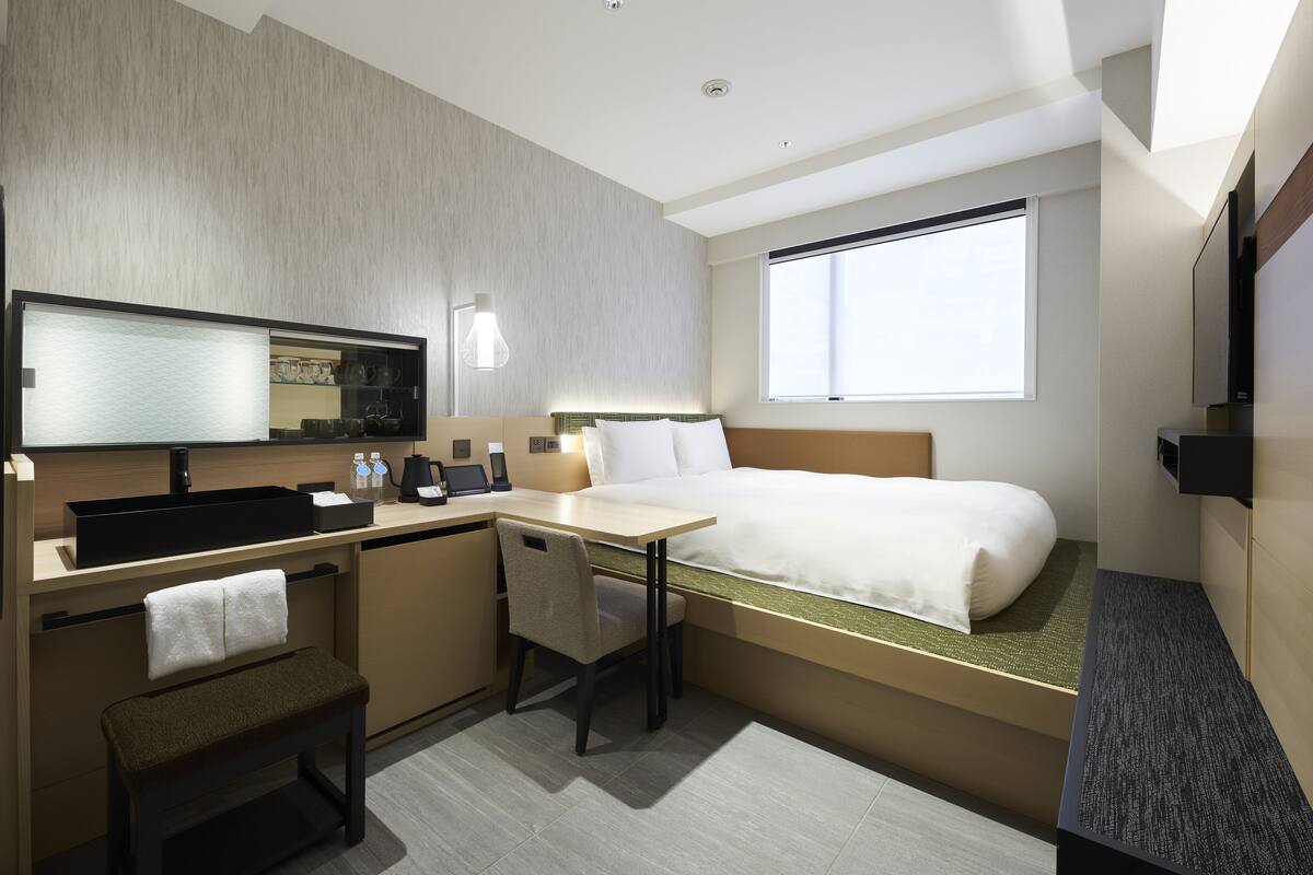 A modern hotel room with a bed, desk, and seating area.