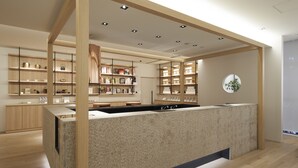 A modern reception area with a central counter, wooden shelving with various items, and a circular wall decoration. - Hotel 1899 Tokyo (Tokyo)