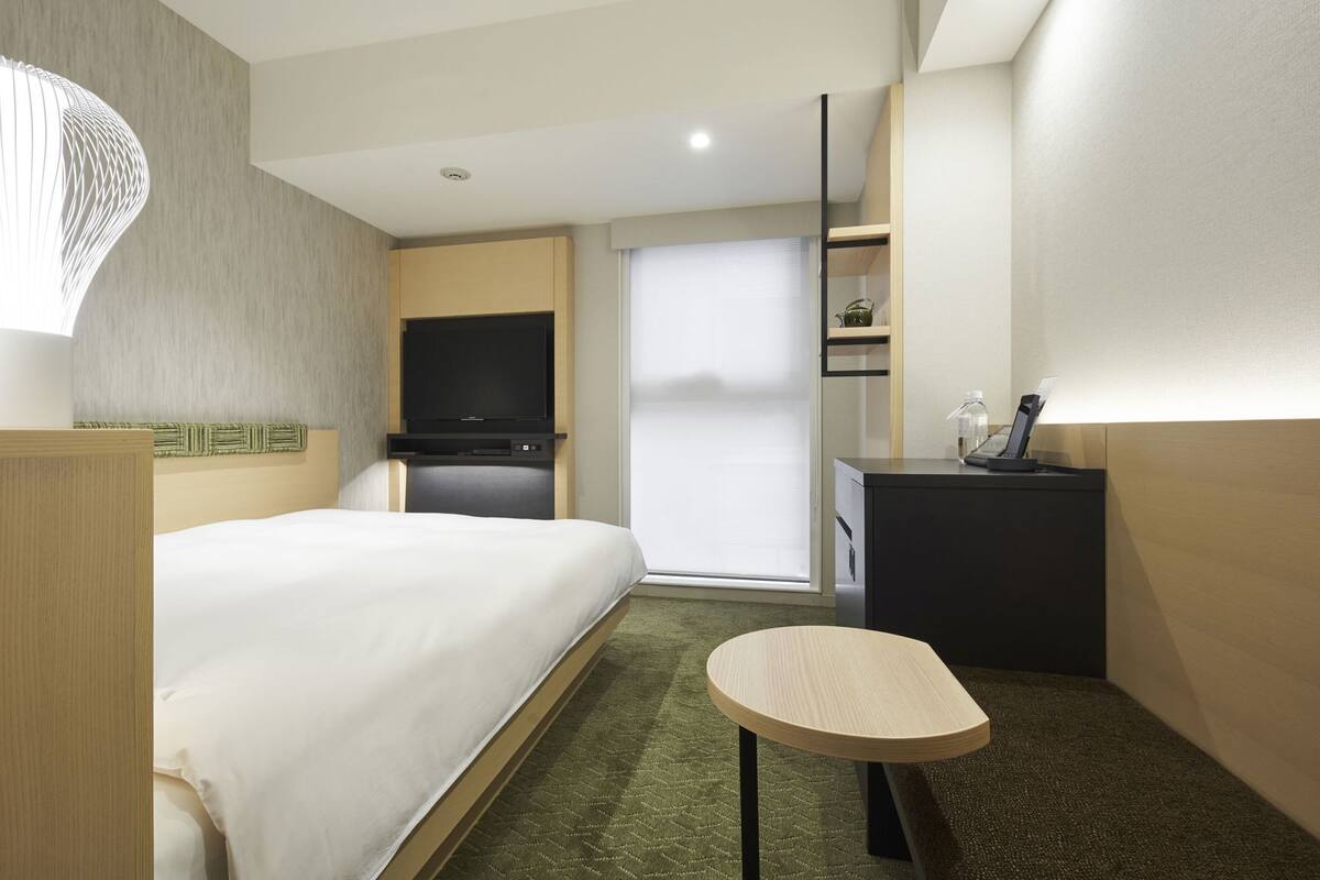 A hotel room with a bed, a desk, a chair, a television, and a window with blinds.