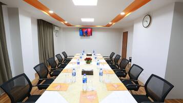 A conference room with a long table, black chairs, water bottles, a clock, and a TV on the wall.