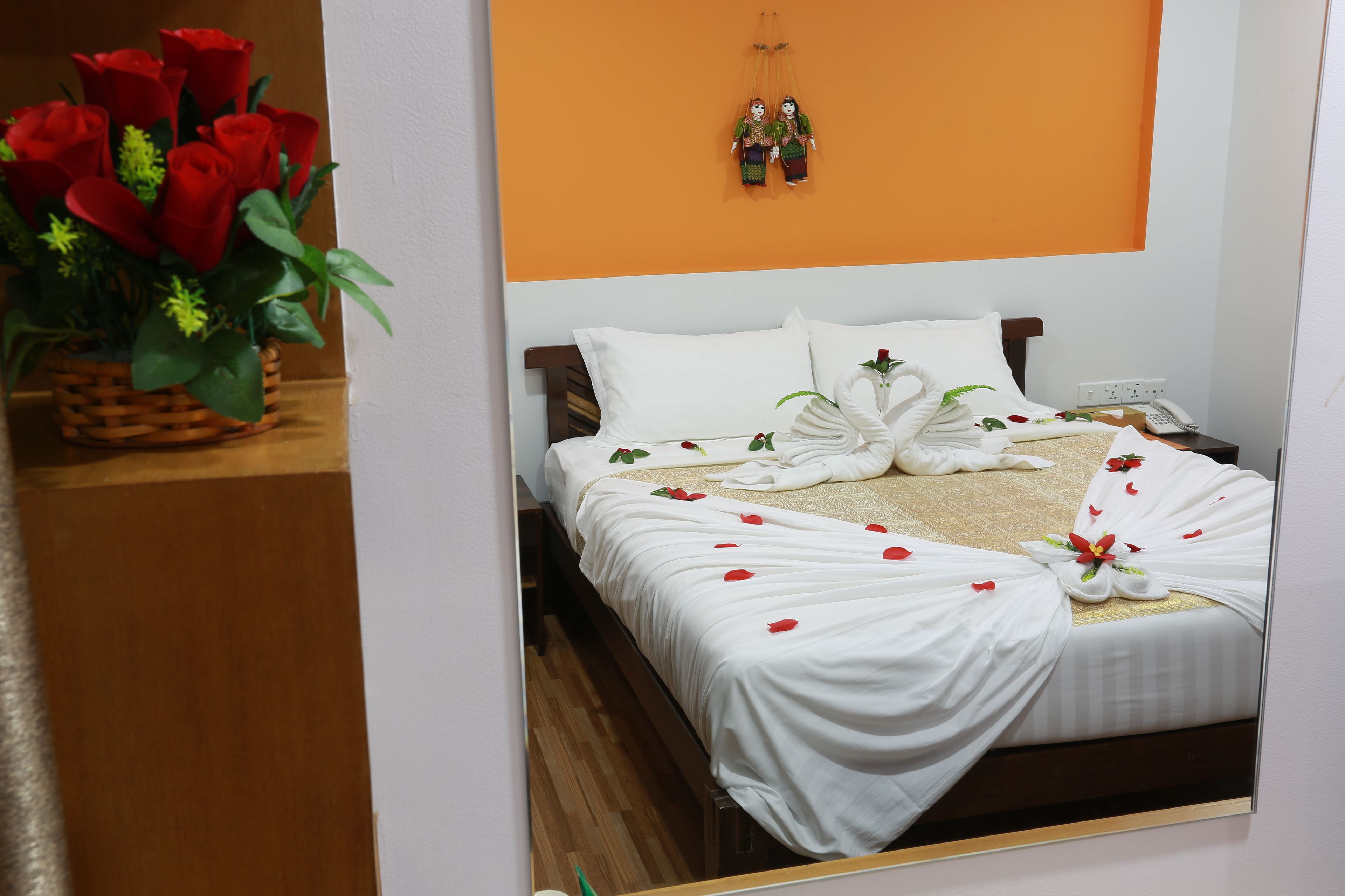 A neatly made bed with white linens, a bouquet of red roses, and a small decorative item on the wall.