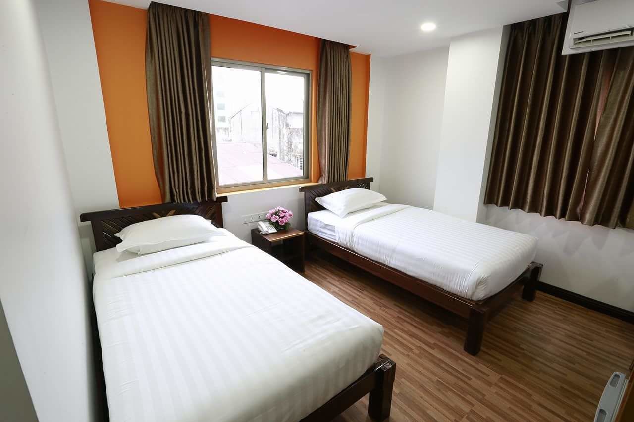 Habitación de hotel con dos camas individuales, una ventana con cortinas, suelo de madera y aire acondicionado.