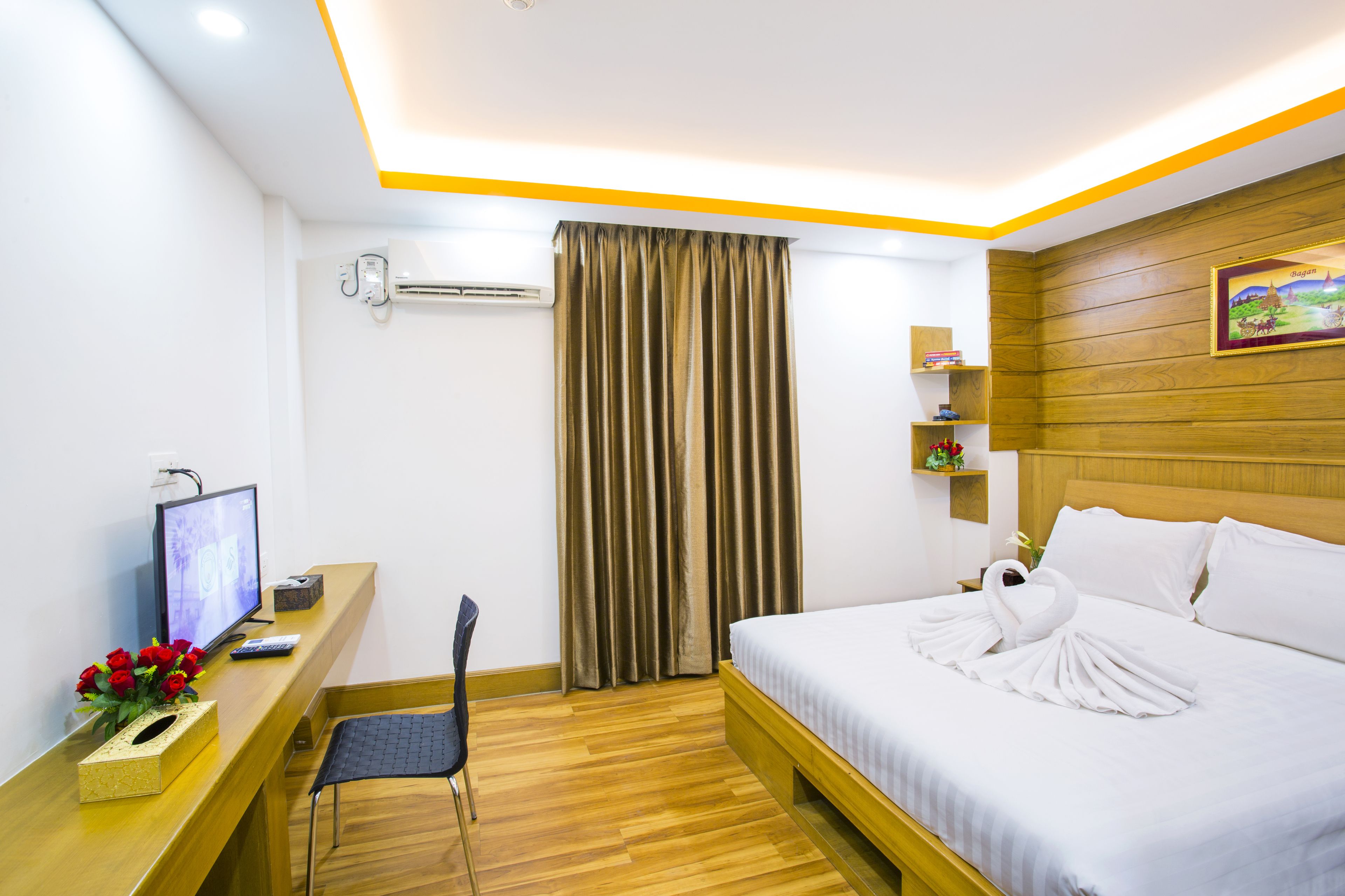 A hotel room with a bed, a desk with a computer monitor, a chair, and a television.