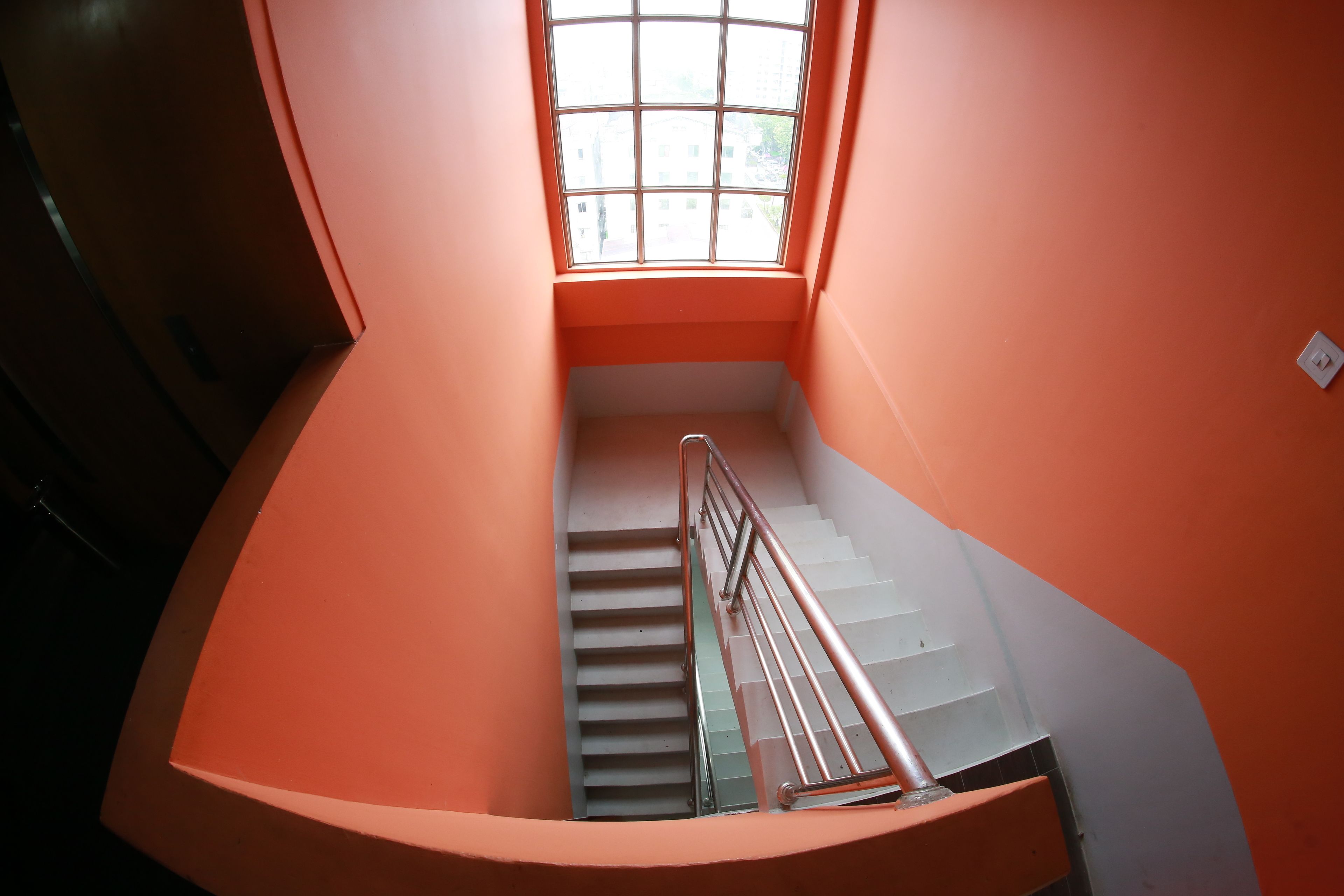 A spiral staircase with a metal handrail, leading to a landing with a large window.