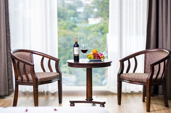 Two wooden chairs with cushioned seats and backs, a round table with a bottle of wine, a glass, and a fruit bowl. - Hotel Vista (Yangon)