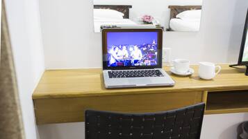 A hotel room with a wooden desk, a laptop, two white cups, and a black chair.