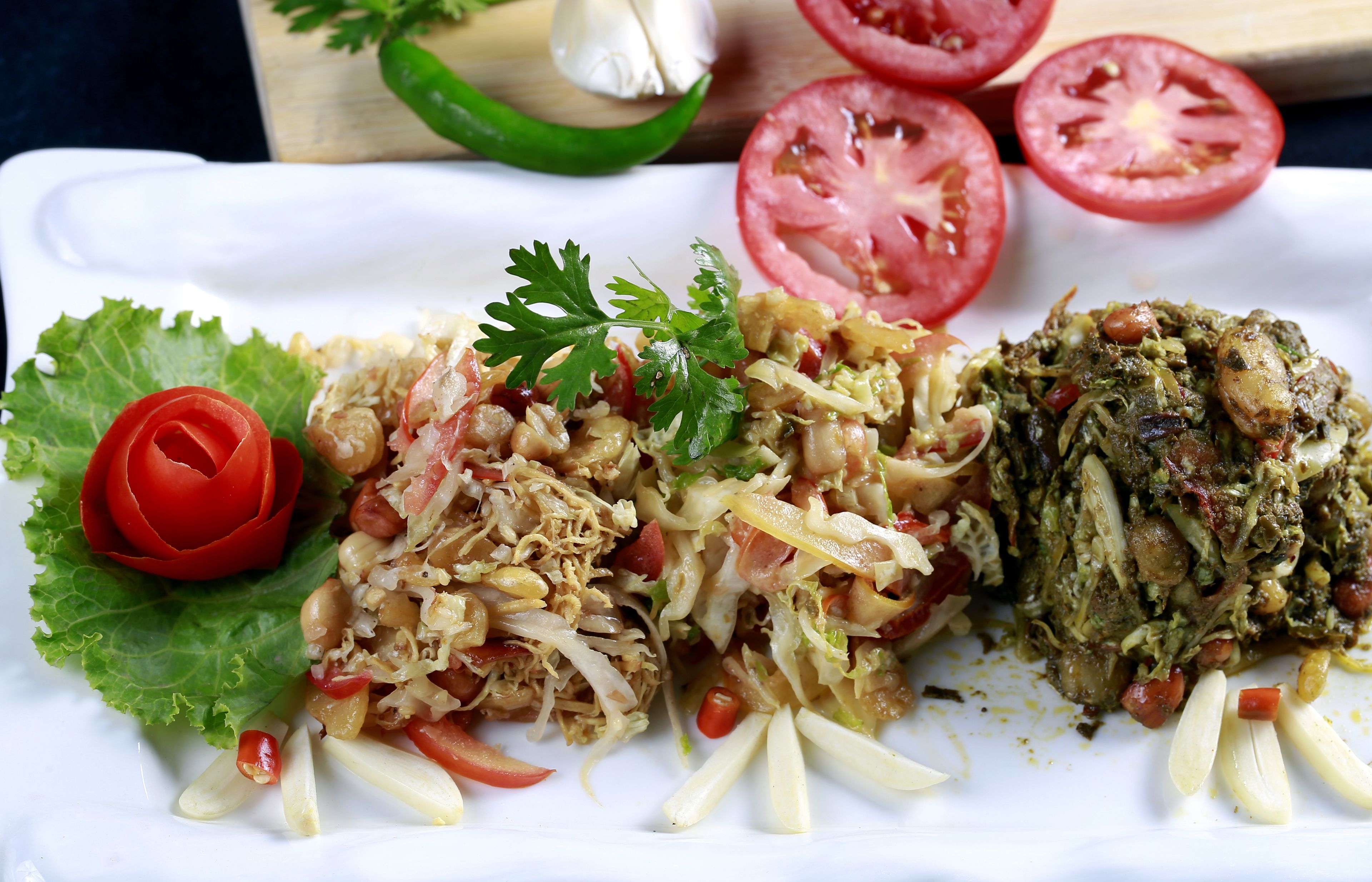 Prato de comida com diversos pratos, incluindo uma salada, um prato de carne e guarnições como alface e tomate.