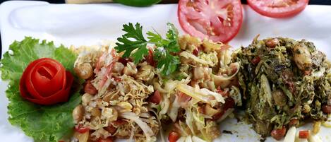 Prato de comida com diversos pratos, incluindo uma salada, um prato de carne e guarnições como alface e tomate.
