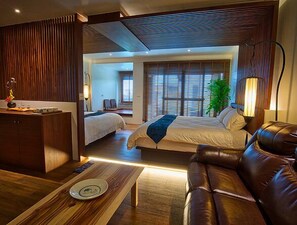 Una habitación de hotel moderna con un escritorio de madera, dos camas, un sofá de cuero y un amplio ventanal con persianas.