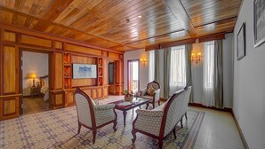 Una habitación amplia con paneles de madera, un ventanal con cortinas, una chimenea y un televisor en la pared.