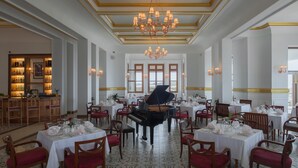 Un salón comedor amplio con un piano de cola, candelabros elegantes y vistas al mar a través de amplios ventanales.