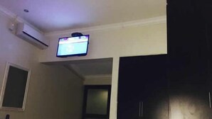A hotel room with a bed, a TV mounted on the wall, and a door leading to another room. - Tsumeb Guesthouse Kamho (Tsumeb)