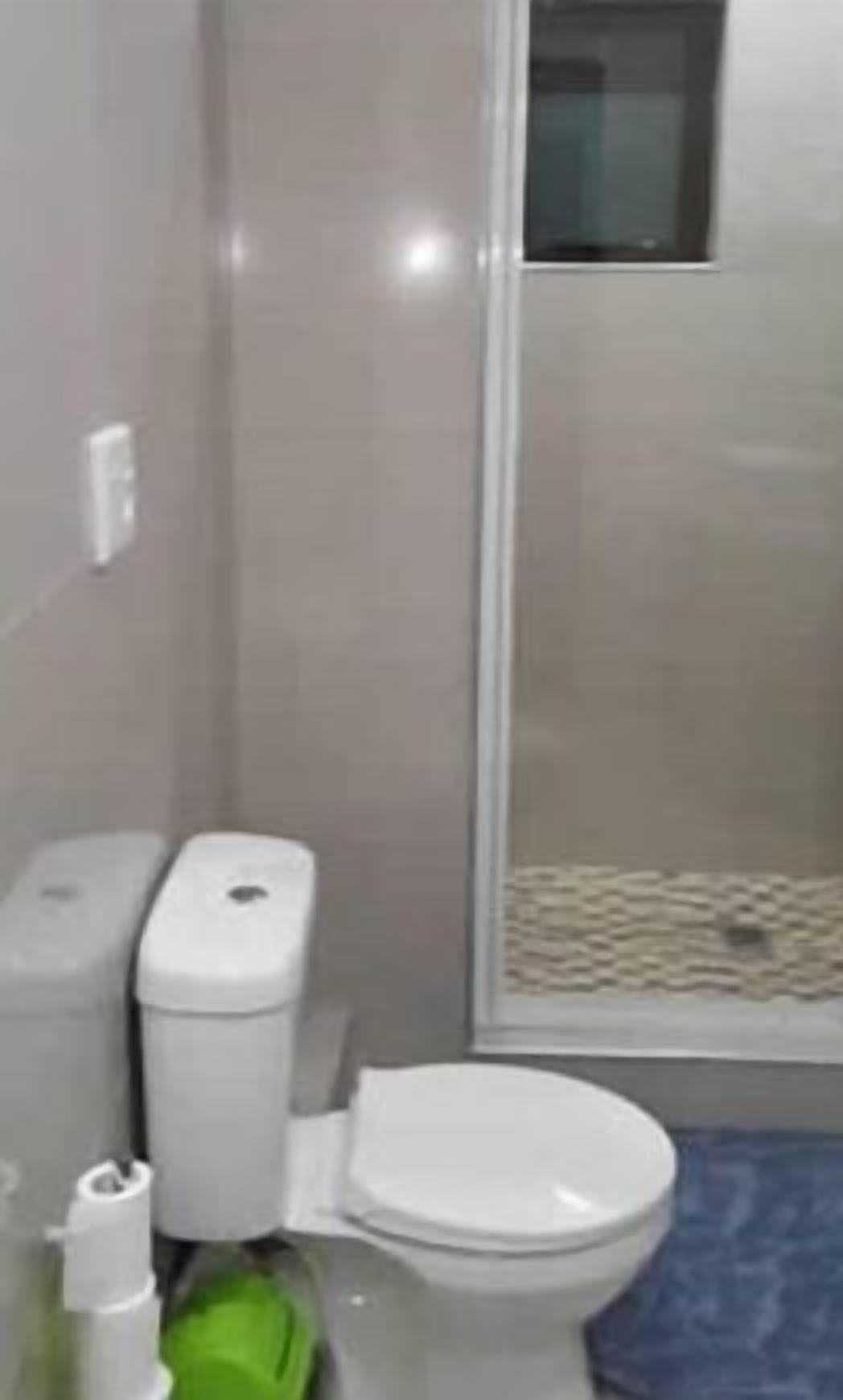 A bathroom with a toilet, a trash bin, and a shower area.