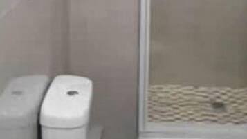 A bathroom with a toilet, a trash bin, and a shower area.