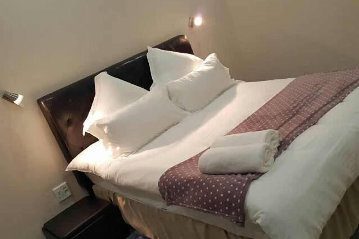 A neatly made bed with white and brown bedding, a brown headboard, and a small bedside table with a lamp.