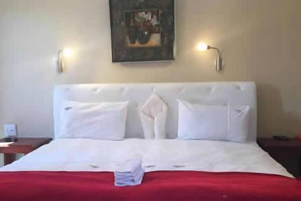 A neatly made bed with a red blanket, white pillows, and a folded towel on the bed.