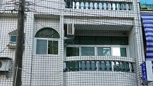 Un immeuble à plusieurs étages, doté d’une façade recouverte de carreaux, d’une entrée abritée et d’un scooter garé devant.