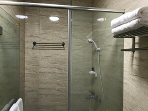 Un box de ducha con paredes de vidrio, un perchero y un estante con toallas.