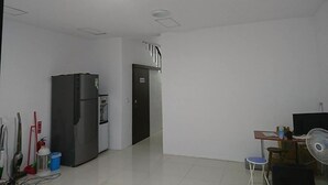 Une cuisine spacieuse équipée d’un réfrigérateur, un coin repas avec une table et des chaises, et un couloir menant à une autre pièce.