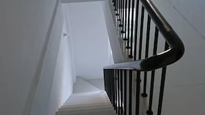 Un escalier aux murs blancs et à la rampe noire, menant à un palier.