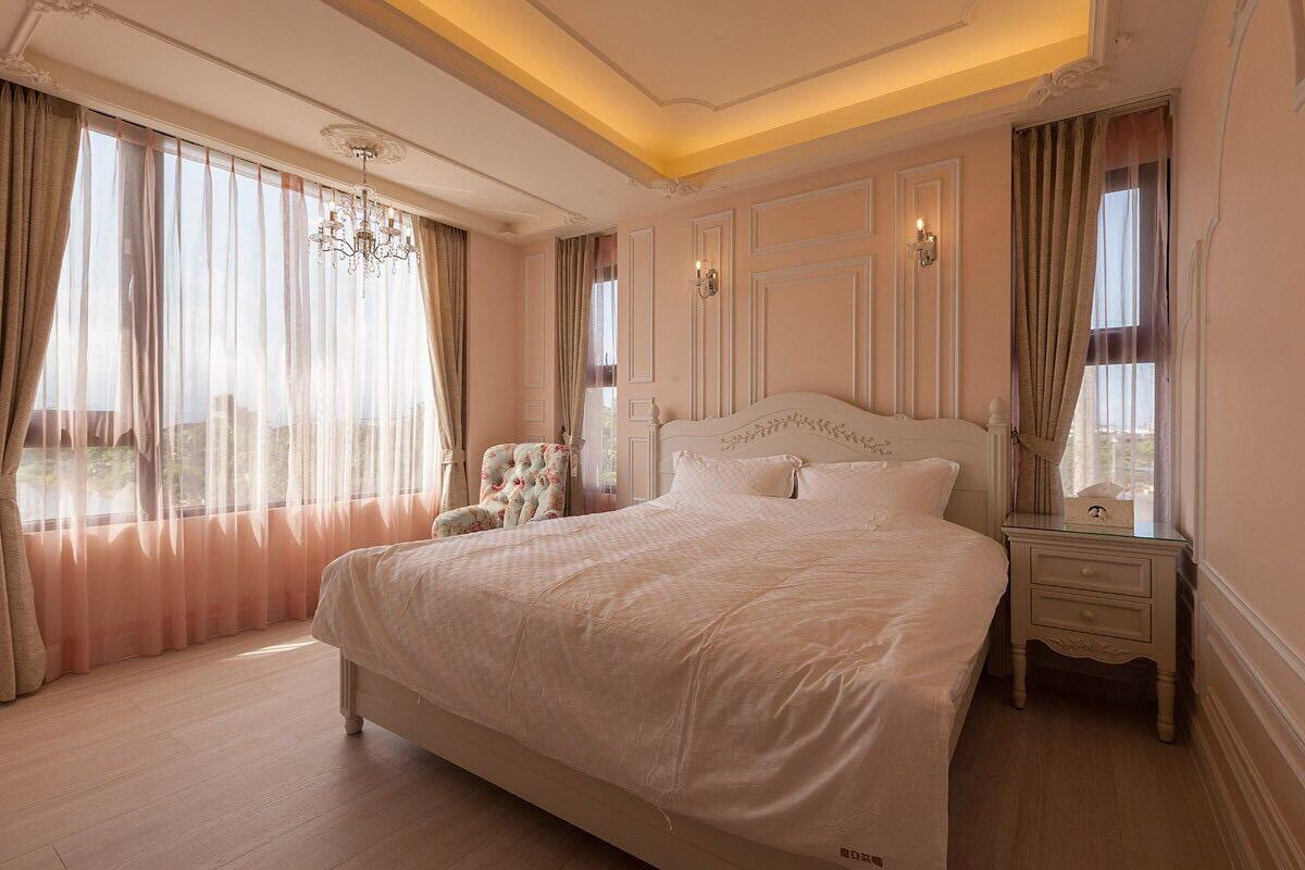 A spacious bedroom with a large bed, a nightstand, a chair, and a chandelier.