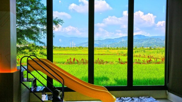 A room with a bed, a window with a view of a green field and mountains, and a yellow chair. - More Manor (Dongshan)