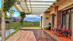 A wooden deck with a pergola, outdoor seating, and a view of a rice field and mountains. - More Manor (Dongshan)
