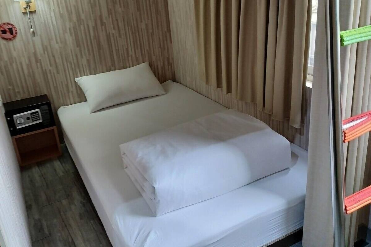 Ein Einzelbett mit weißer Bettwäsche in einem Zimmer mit Holzboden und beigen Vorhängen.
