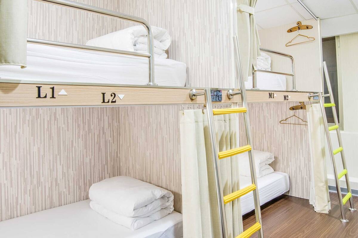 Ein Hotelzimmer mit Stockbetten, die mit L1 und L2 beschriftet sind, einem Holzboden und einem Spiegel an der Wand.