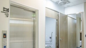 Un ascensor moderno con panel de control, puerta de madera y un pasillo que lleva a una habitación con cama y ventana.