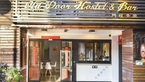 La entrada del Old Door Hostel & Bar, con fachada de madera, un letrero y suelo de baldosas.