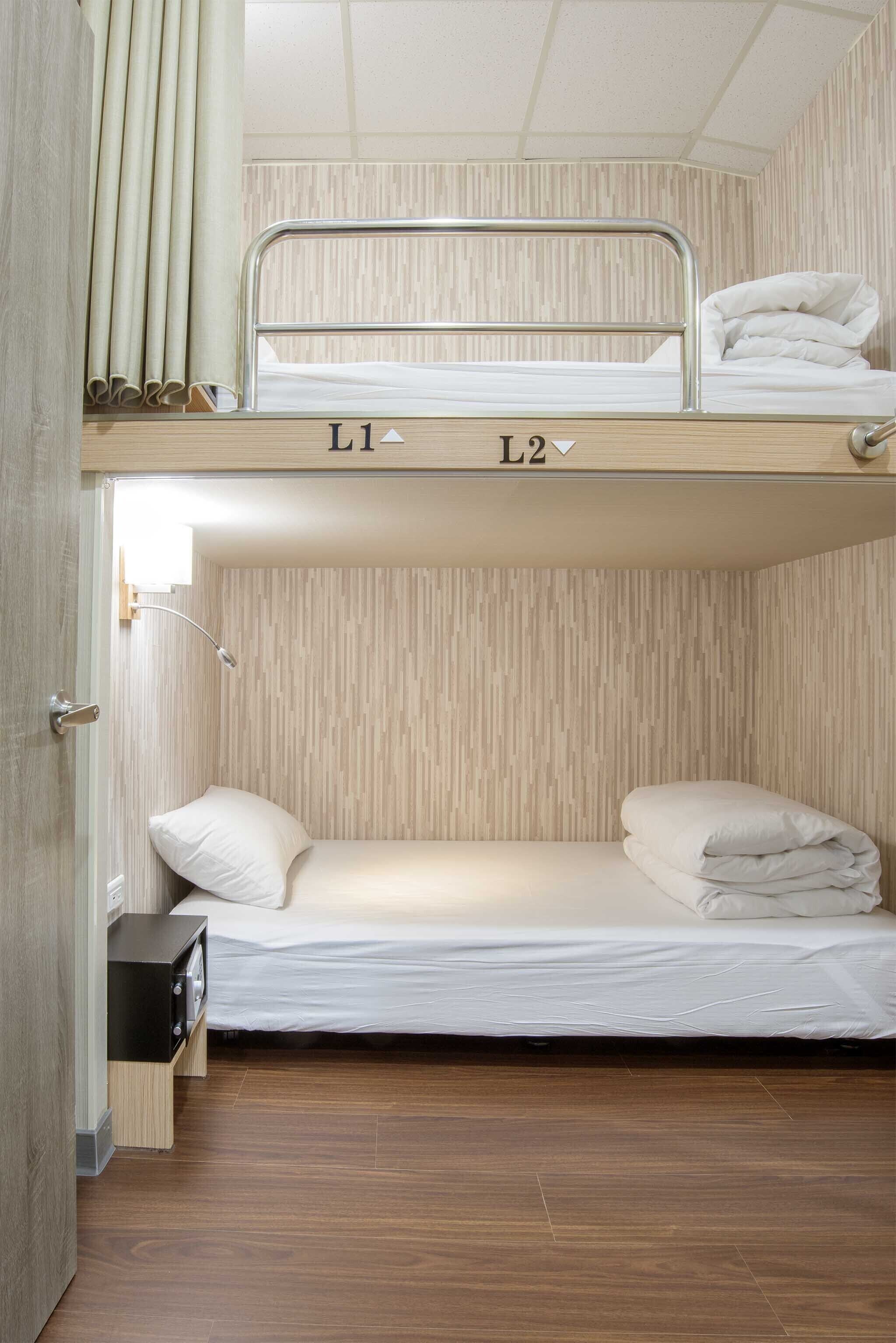 A bunk bed with two labeled sections, L1 and L2, in a room with wooden flooring and a wall-mounted lamp.