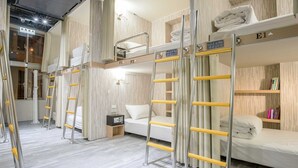 Habitación de hotel con literas, un escritorio, una silla, una mesita de noche y una estantería.