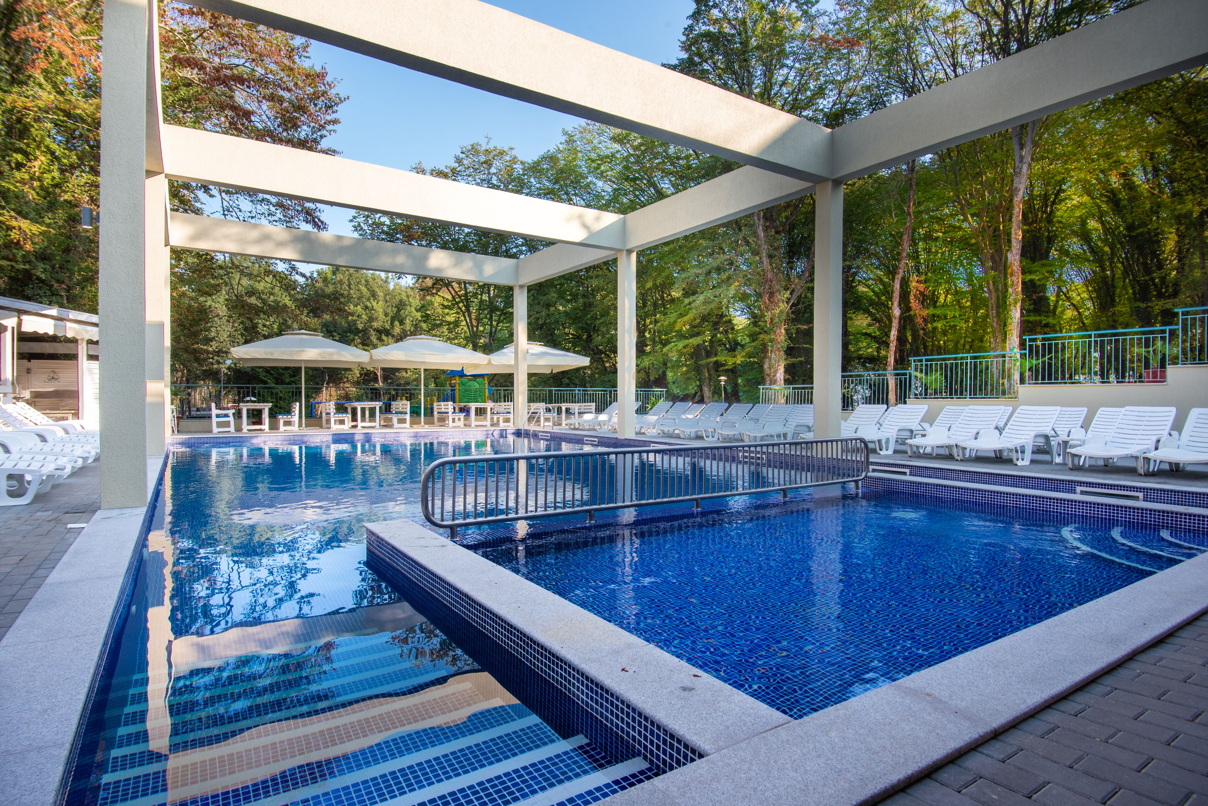 A swimming pool with a tiled deck, lounge chairs, and umbrellas.
