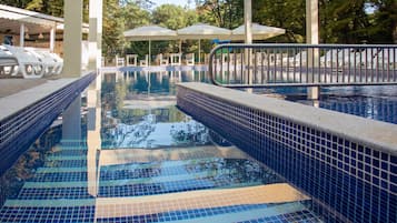 Una piscina al aire libre, sombrillas, sillones reclinables de piscina