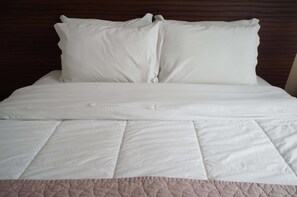 Una cama bien hecha con ropa blanca y una parte inferior acolchada.