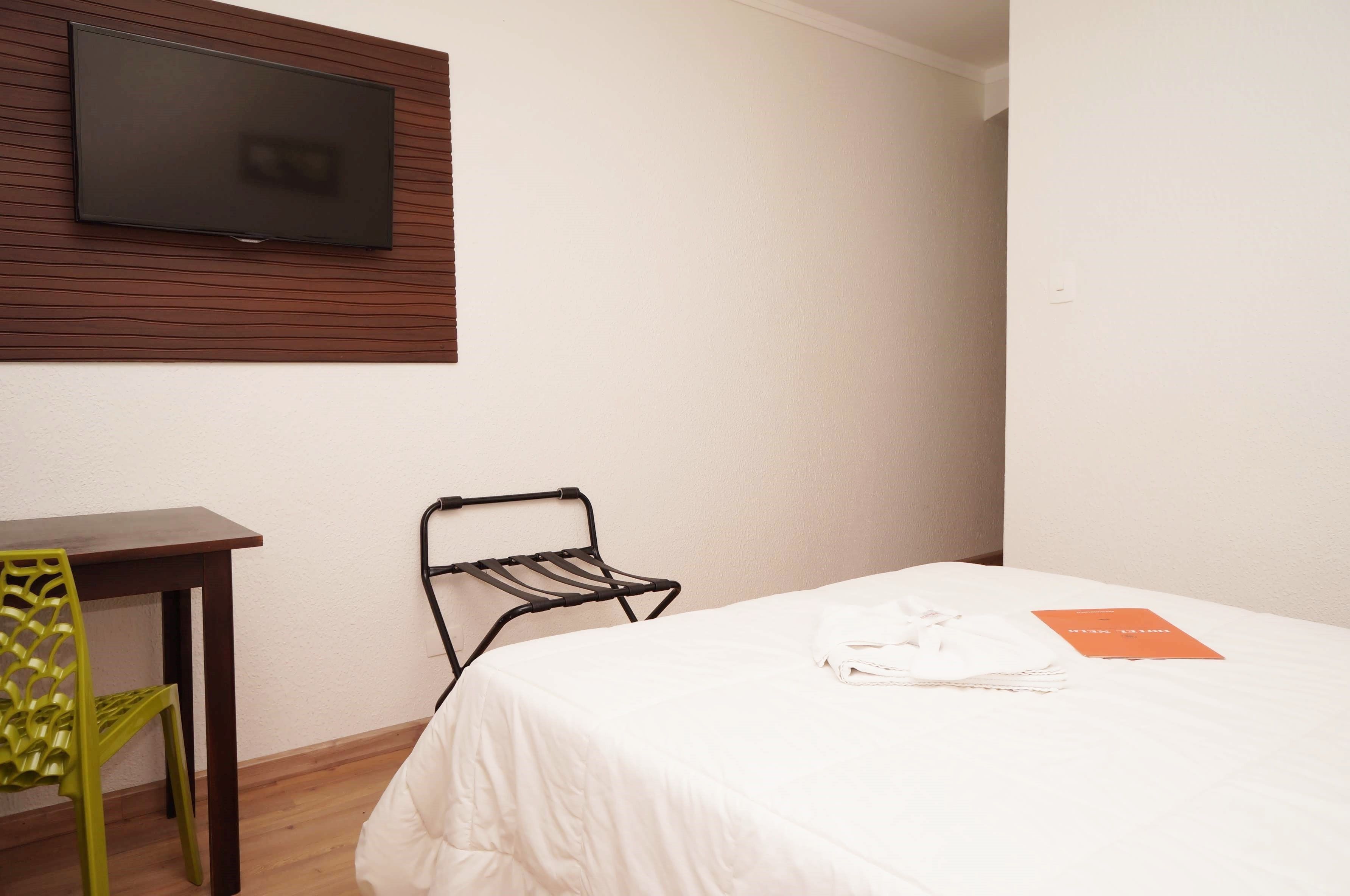 A hotel room with a bed, a TV mounted on the wall, a small table, and a chair.
