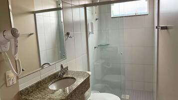 A bathroom with a granite countertop sink, a white toilet, a glass shower enclosure, and a hairdryer mounted on the wall.