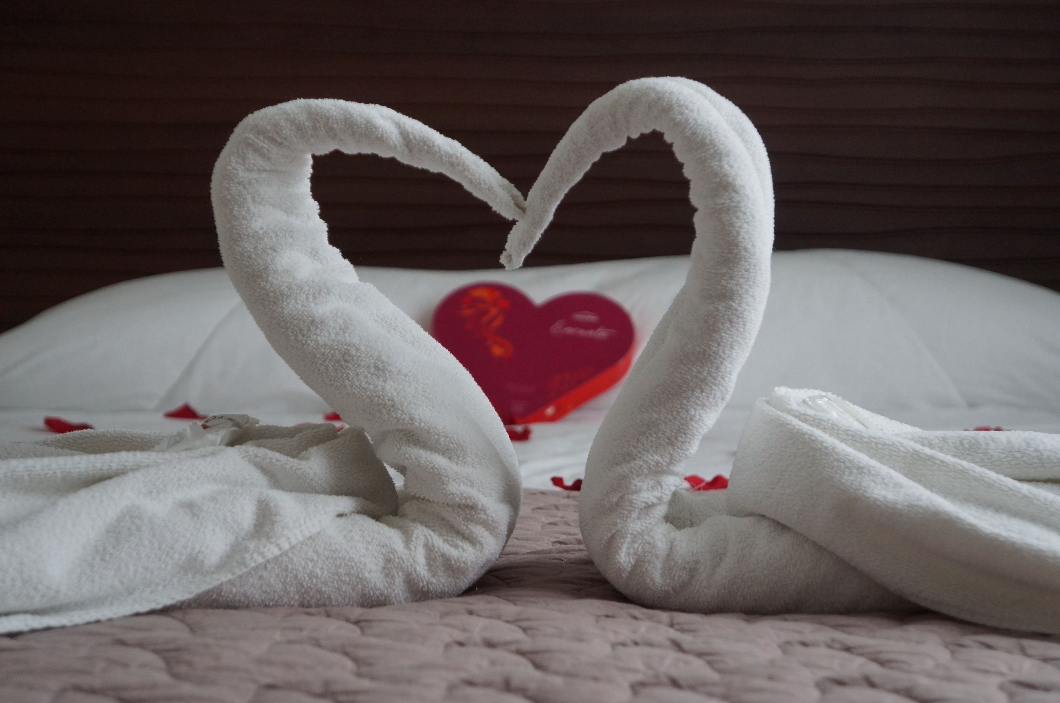 Una cama con un cojín con forma de corazón y dos toallas con forma de cisne.