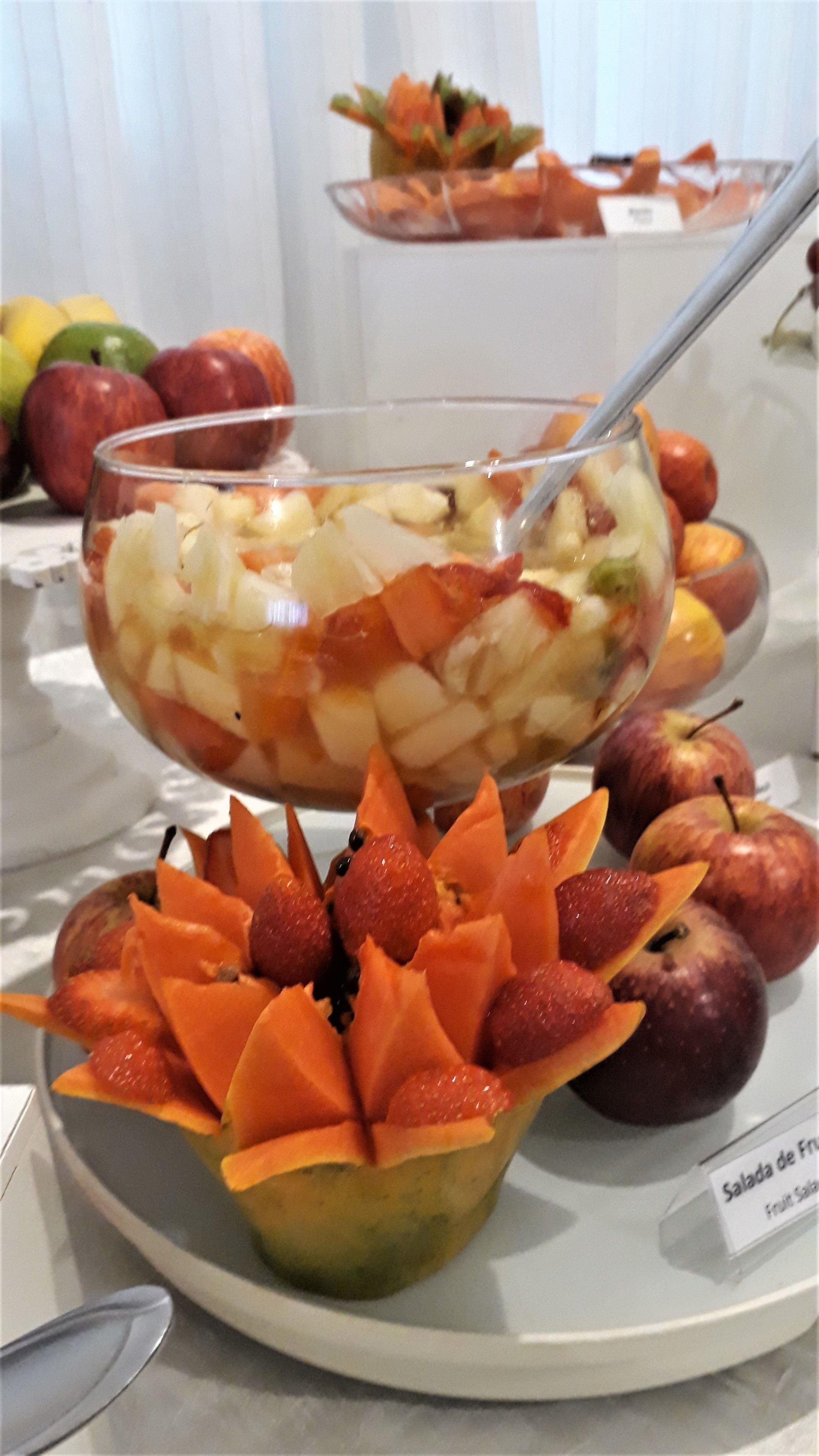Un bol de amanida de fruita amb una cullera, envoltat de pomes i una composició decorativa de fruita.