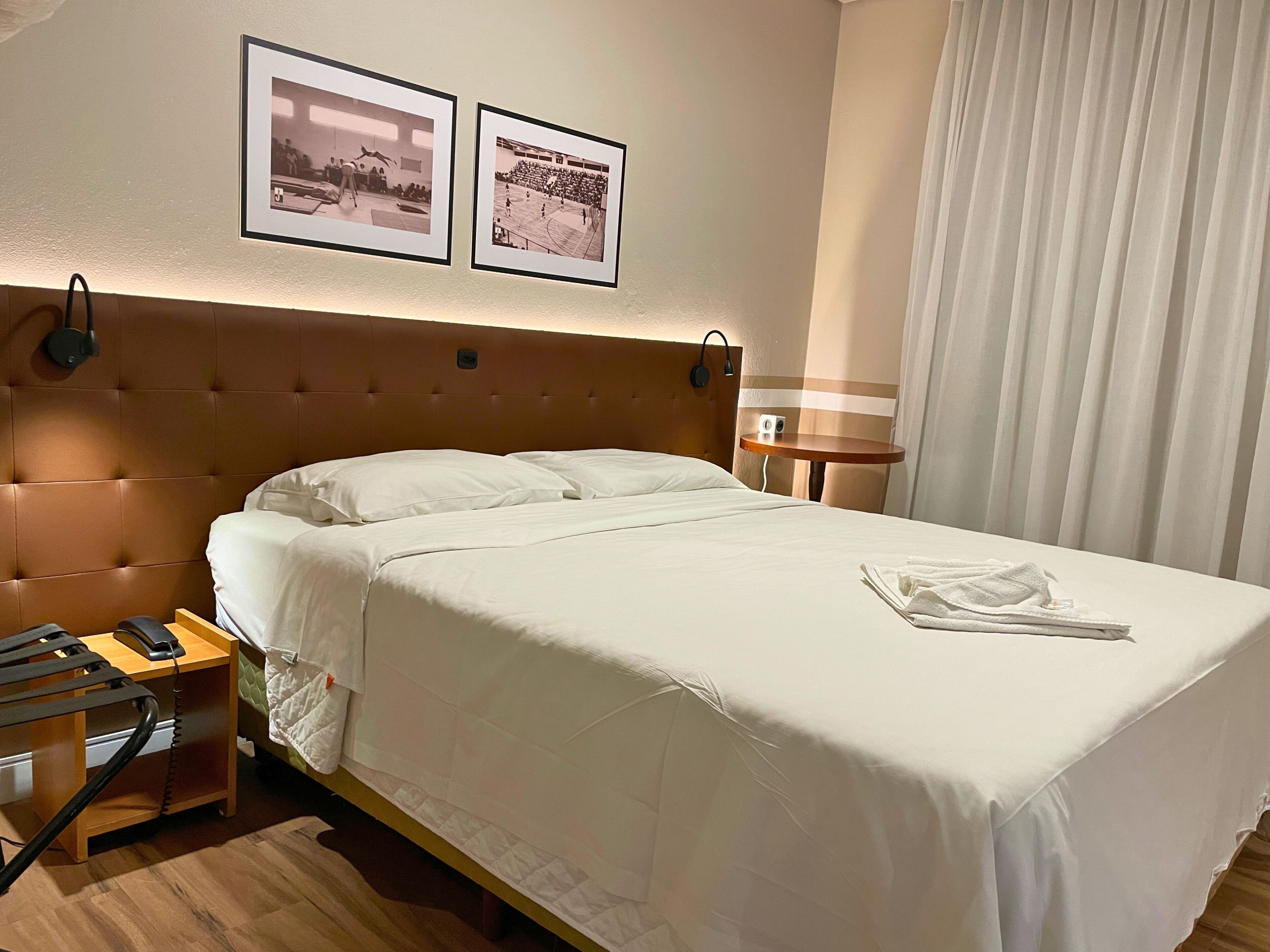 A hotel room with a large bed, a bedside table with a phone, a lamp, and two framed pictures on the wall.