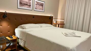 A hotel room with a large bed, a bedside table with a phone, a lamp, and two framed pictures on the wall.